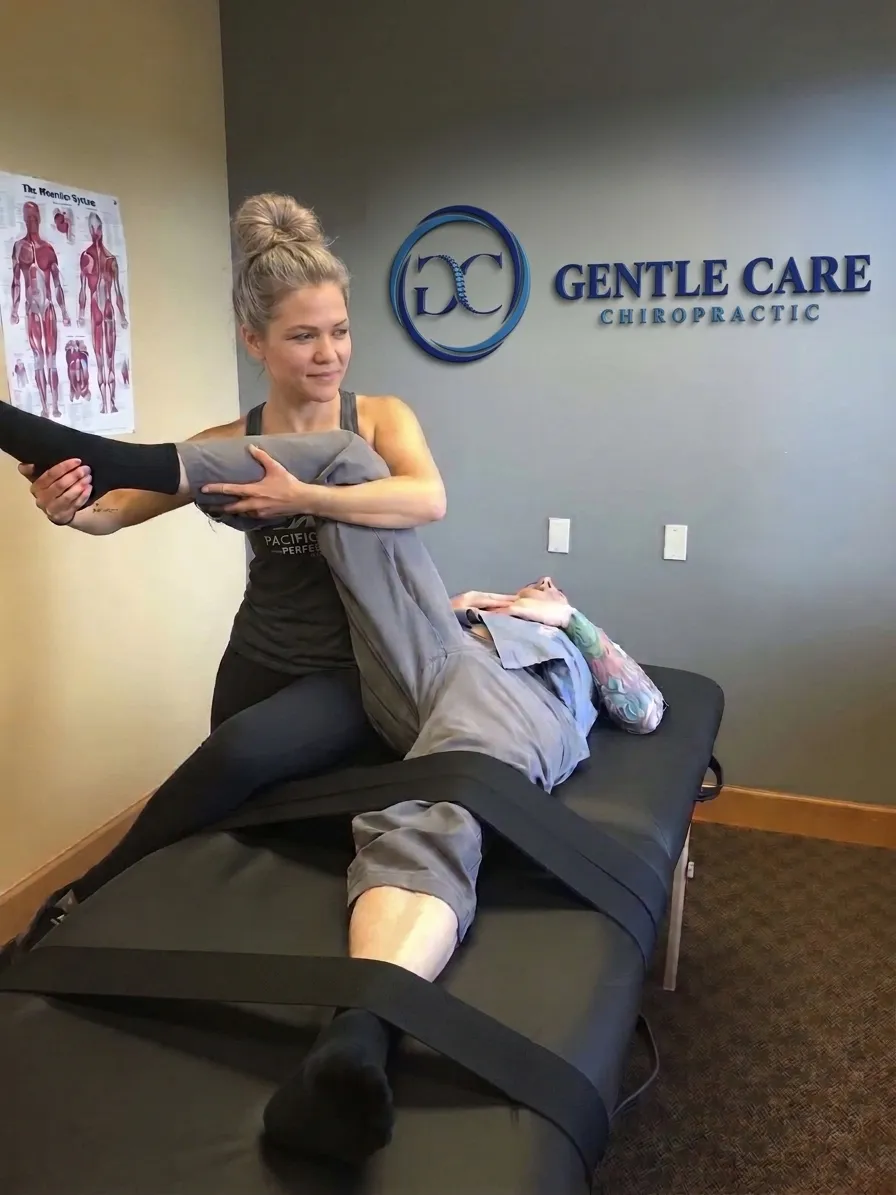 Stretch therapist guiding a client through a deep hip and leg stretch with support straps on a treatment table